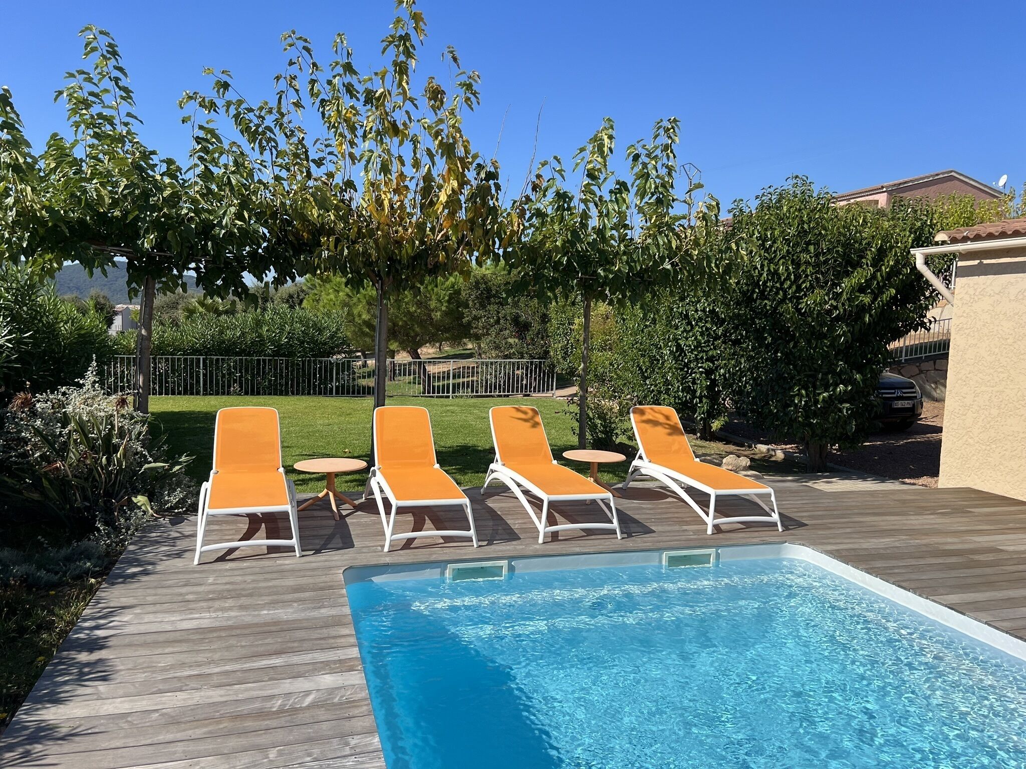 Ein Swimmingpool mit vier orangefarbenen Liegestühlen und einem kleinen runden Tisch.