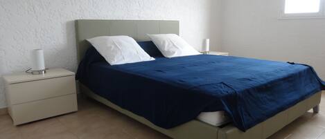 Un lit avec une couvre-lit bleue, deux oreillers blancs et une table de chevet avec une lampe.