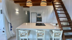 Een moderne keuken met een centraal eiland, witte stoelen en een houten trap.