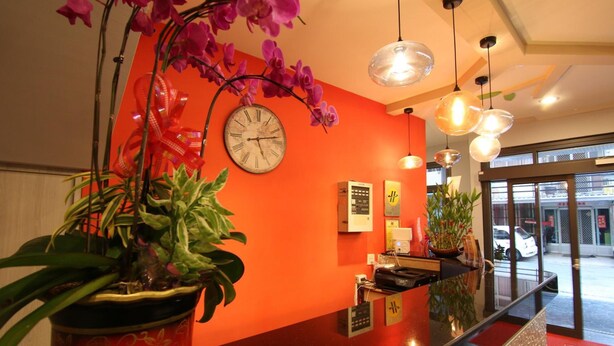 A reception area with a red wall, a clock, and potted plants. - Prince To Travel Hotel (Chiayi City)