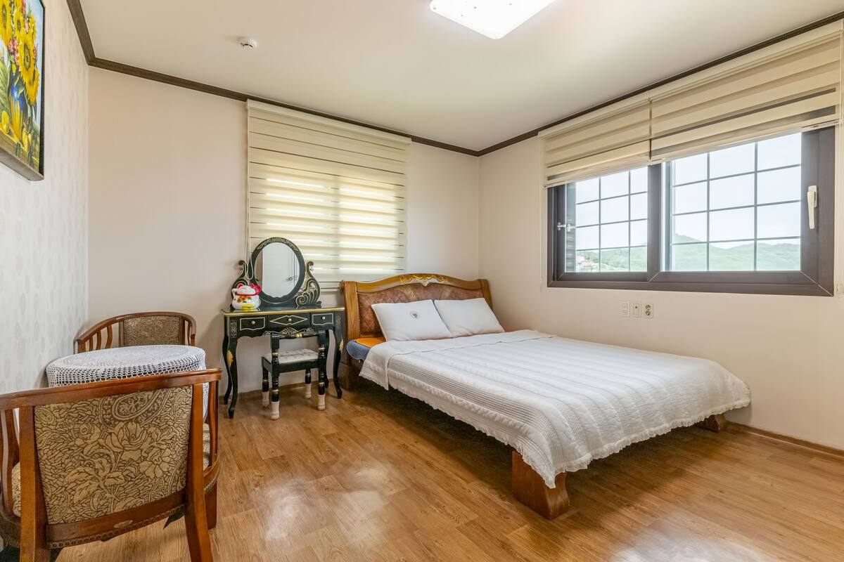 Un dormitorio con una cama de madera, un escritorio con silla, una ventana con persianas y un cuadro en la pared.