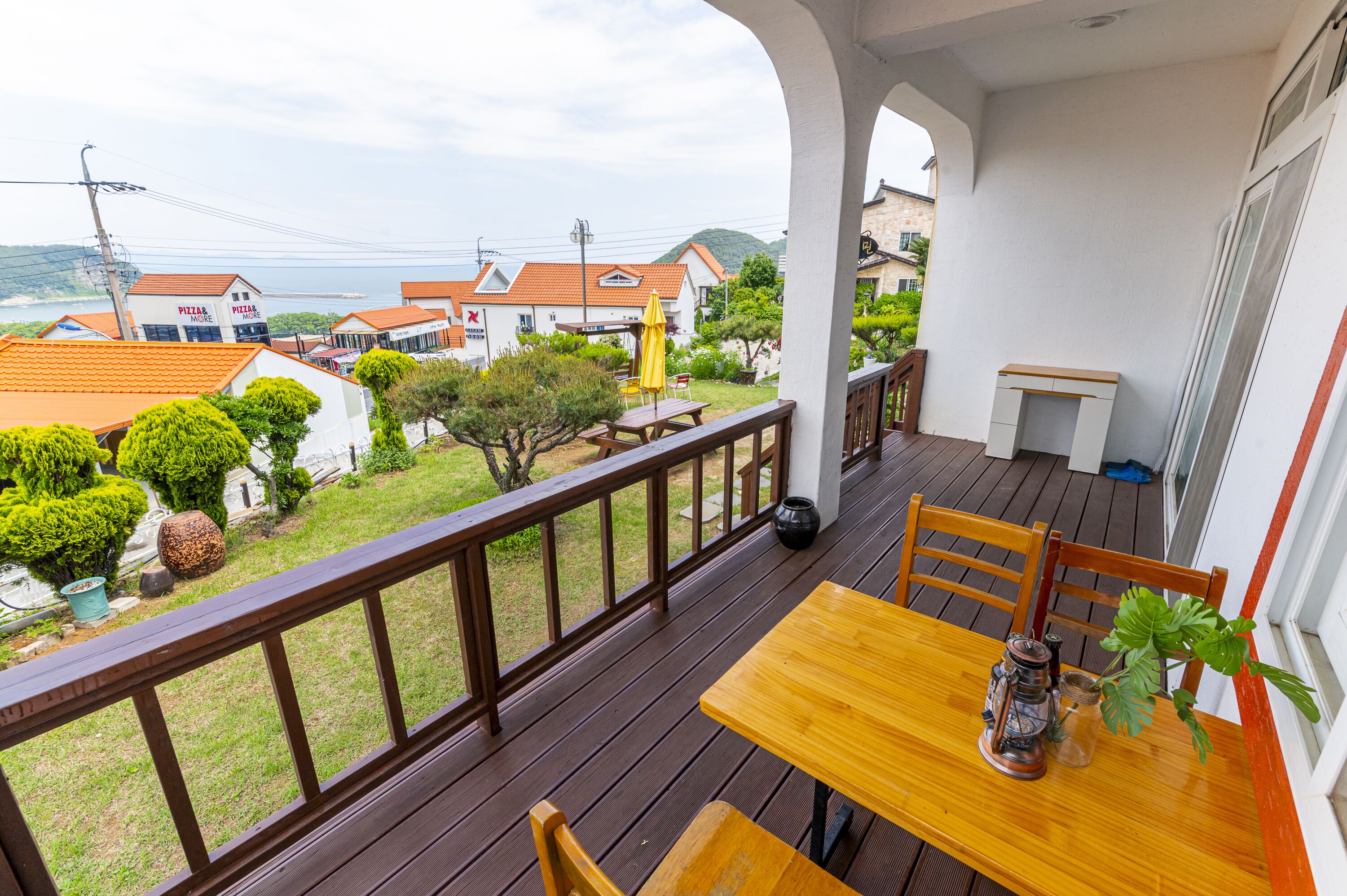A wooden deck with a table and chairs, overlooking a residential area with houses and a view of the sea.