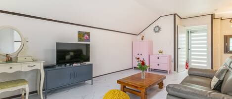 A living room with a TV, a wooden coffee table, a sofa, a pink cabinet, and a yellow pouf.