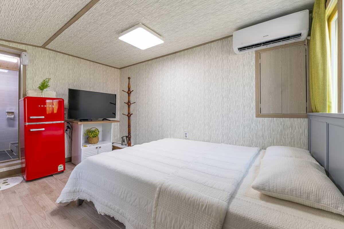 Un dormitorio con una cama, un refrigerador rojo, un televisor y un equipo de aire acondicionado.