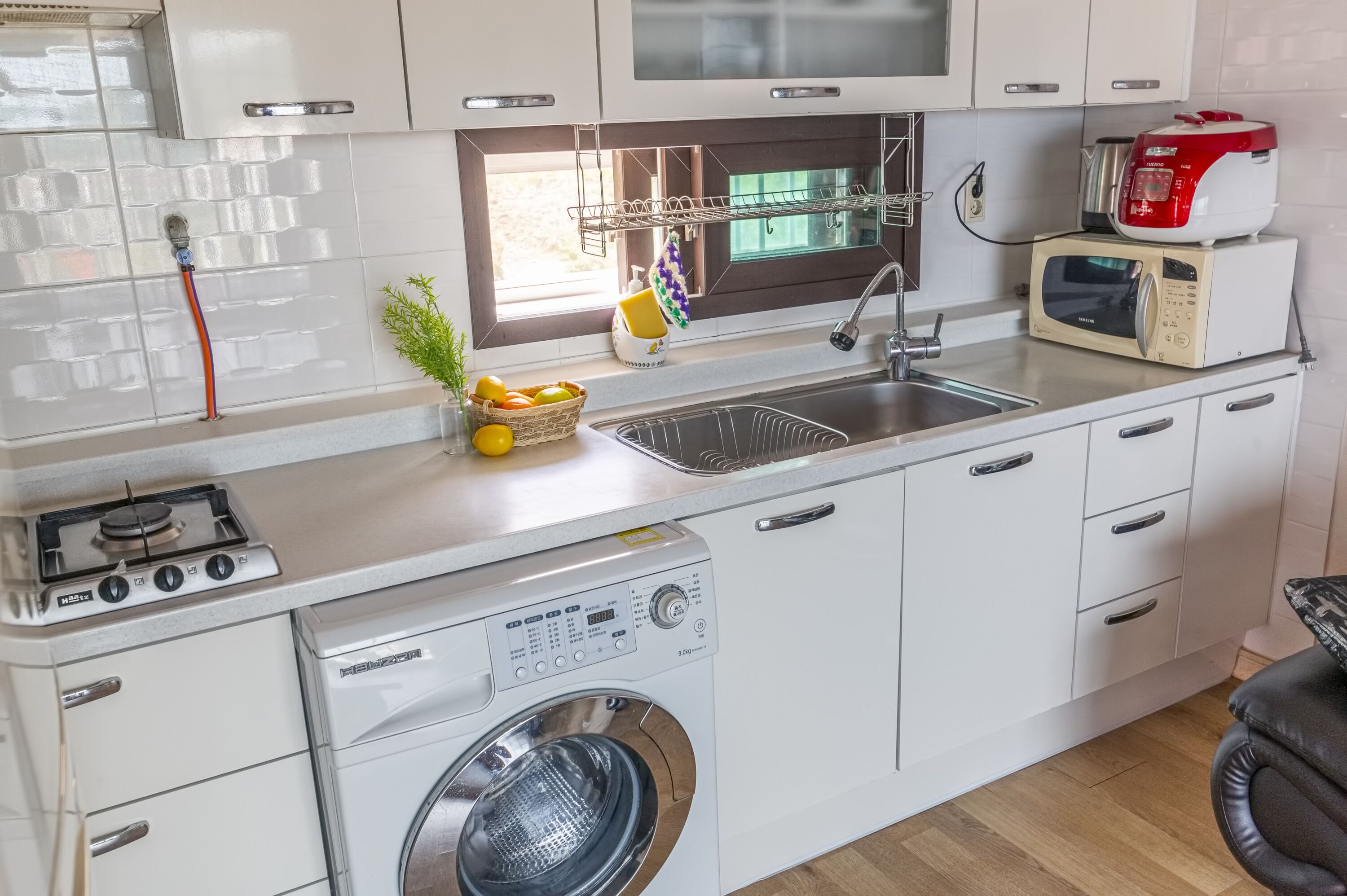 Une cuisine compacte équipée d’une cuisinière à gaz, d’un four à micro-ondes, d’un évier et d’un lave-linge encastré.