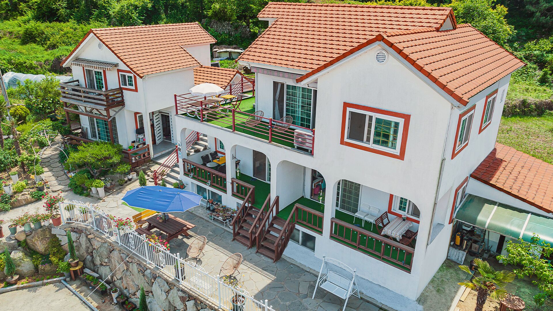 Un immeuble à plusieurs étages, doté d’un toit recouvert de tuiles rouges, de balcons et d’un patio aménagé avec du mobilier d’extérieur.