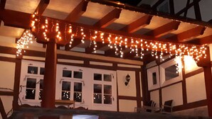 A building with a wooden structure and white walls, featuring multiple windows and a balcony area with string lights.