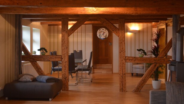 A cozy living room with a wooden ceiling, a dining area with a table and chairs, and a staircase leading to another level.