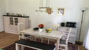 Una cocina moderna con armarios blancos, una mesa de comedor con sillas, un banco, un microondas y un refrigerador pequeño.