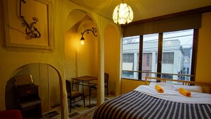 A bedroom with a bed, a desk, a chair, a piano, and a window with a view of buildings. - Hakuba Station Guest House Hostel eN (Hakuba)