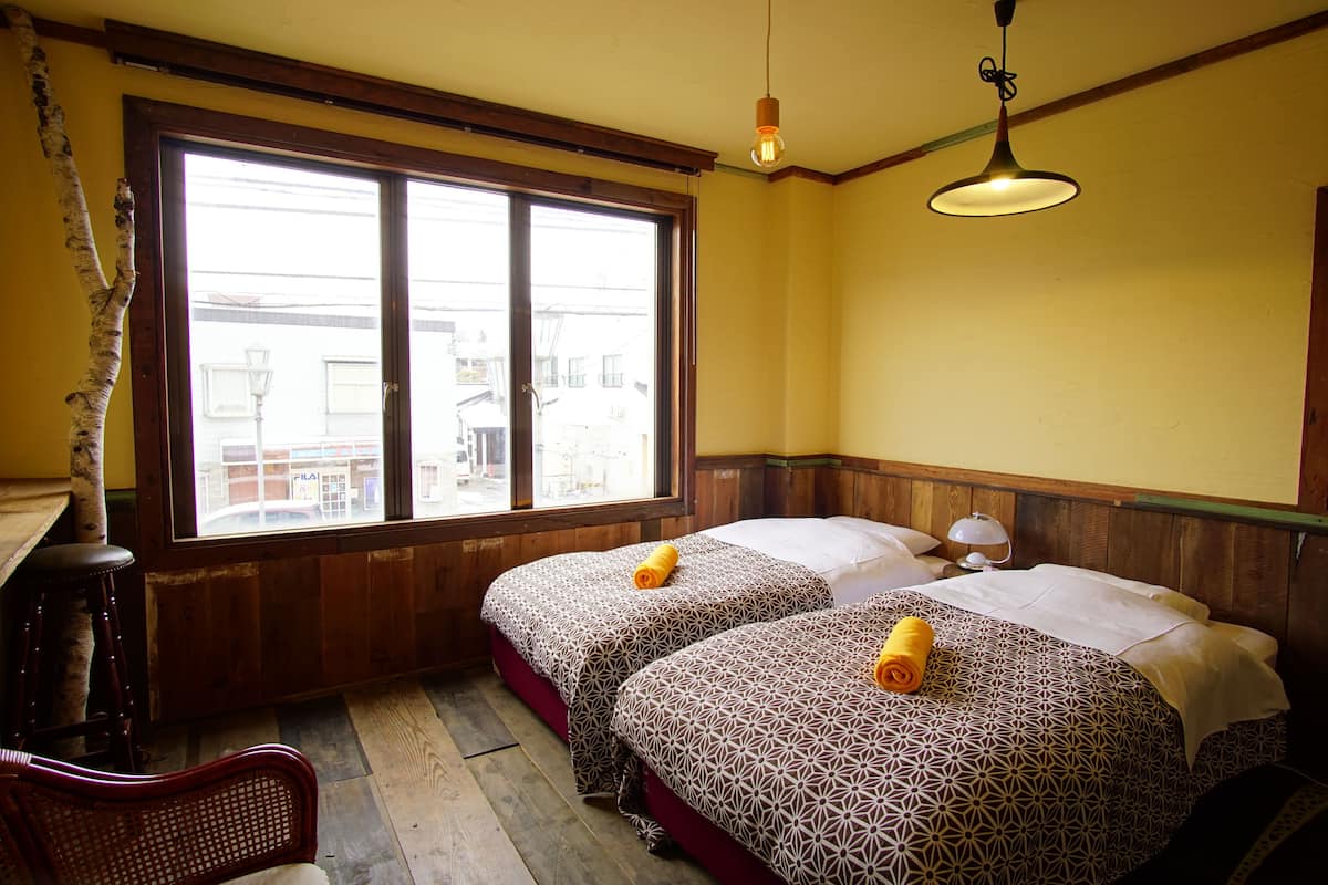 A hotel room with two beds, a wooden chair, a large window, and a hanging light fixture.