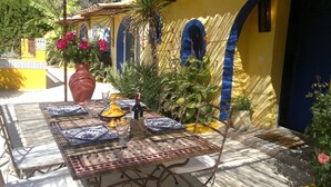 An outdoor dining area with a table set for two, featuring blue and white patterned tableware, a large vase with flowers, and a bottle of wine. - Gîte Le RIAD quiet vacation home swimming pool and jacuzzi garden Carpentras (Carpentras)