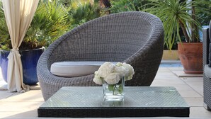 A wicker chair with a cushion, a glass table with a vase of flowers, and potted plants in the background. - Atypical house in the south of Provence near Avignon, 4 persons   (Carpentras)