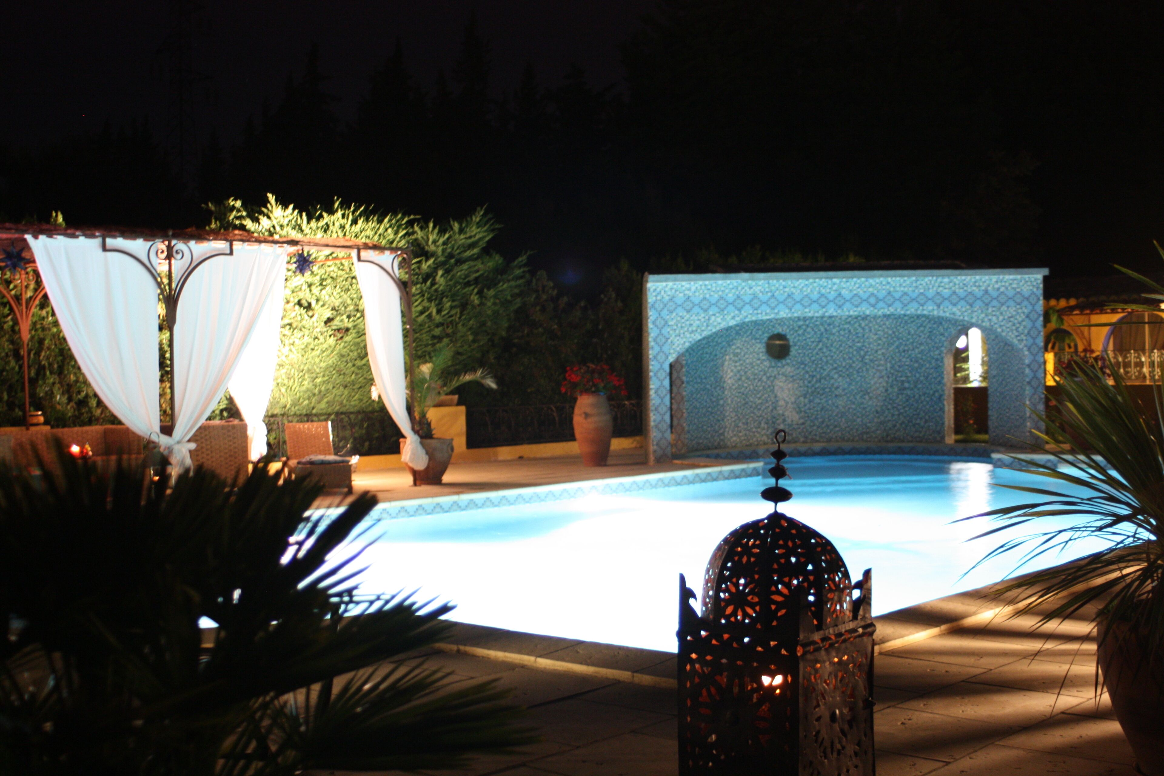 Ein Poolbereich bei Nacht mit klarem Pool, einer dekorativen Laterne und einer gefliesten Struktur im Hintergrund.