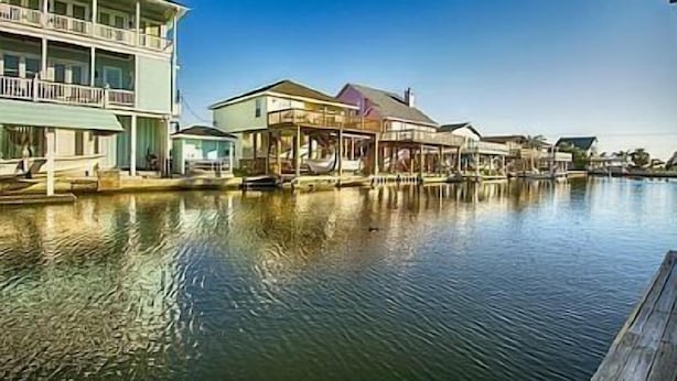 Een pand aan het water met meerdere gebouwen, waaronder een groot huis met balkon en een kleiner gebouw met overdekte veranda.