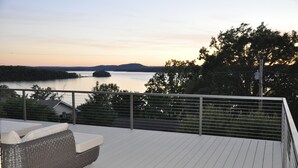 A deck with a wicker sofa and a view of a lake at sunset.