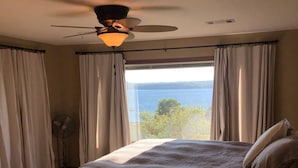 A bedroom with a large bed, a ceiling fan, and a view of a lake.