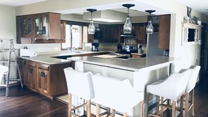 A modern kitchen with wooden cabinets, a large island with bar stools, pendant lighting, and a stainless steel refrigerator.