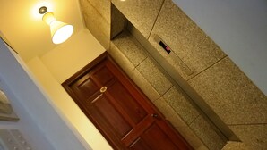 A wooden door with a brass handle and a number plate, a wall-mounted light fixture, and a textured stone wall. - Smiley Apartment 3 (Ho Chi Minh City)