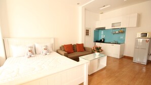 A bedroom with a bed, bedside tables, a sofa, and a kitchenette with a microwave and refrigerator. - Smiley Apartment 3 (Ho Chi Minh City)