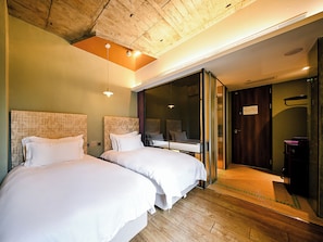 Habitación de hotel con dos camas, techo de madera y una puerta corrediza de vidrio que da a un baño.