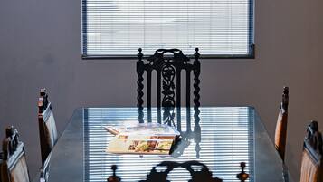 Una mesa de comedor con sillas, una ventana con persianas y una revista sobre la mesa.