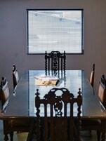 Una mesa de comedor con sillas, una ventana con persianas y una revista sobre la mesa.