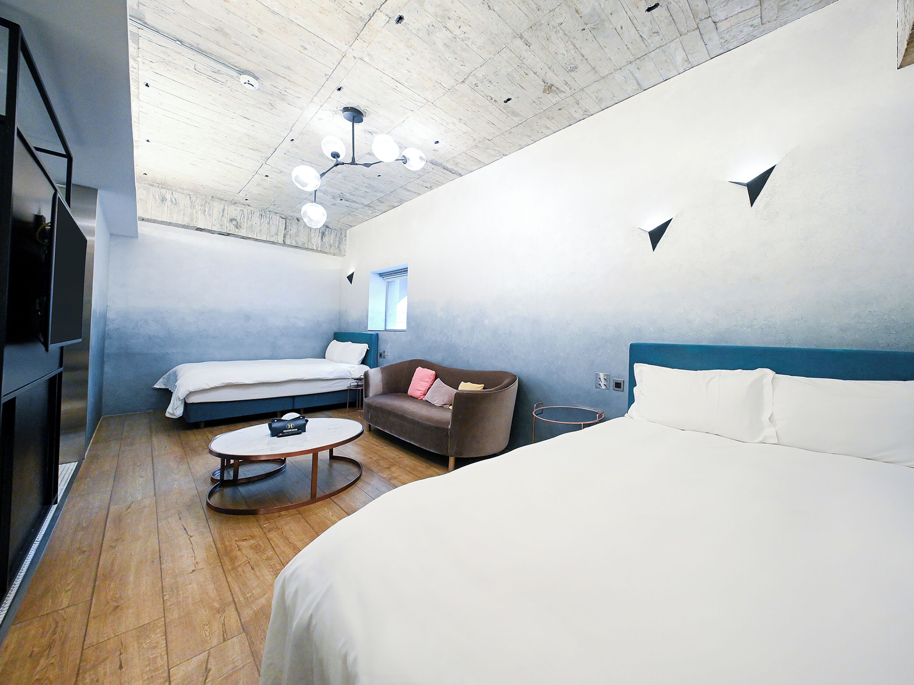 A modern hotel room with a large bed, two smaller beds, a sofa, a coffee table, and a TV.