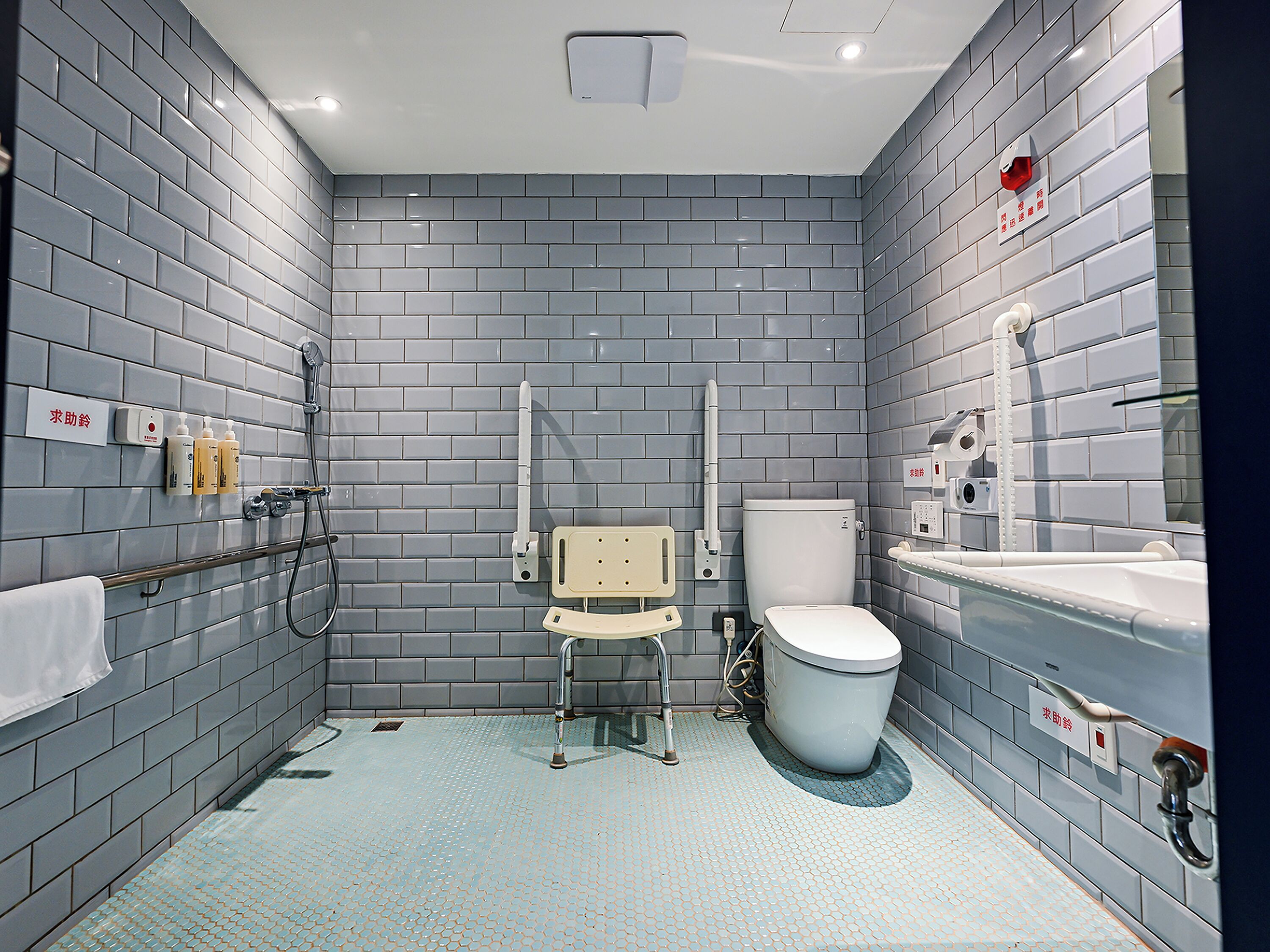 A modern bathroom with grey tiled walls, a white toilet, a sink, and a shower area.
