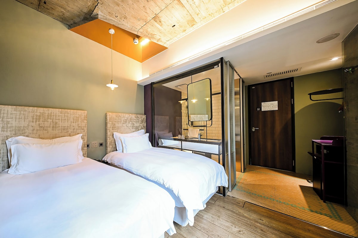 Habitación de hotel con dos camas, un baño con espejo y piso de madera.
