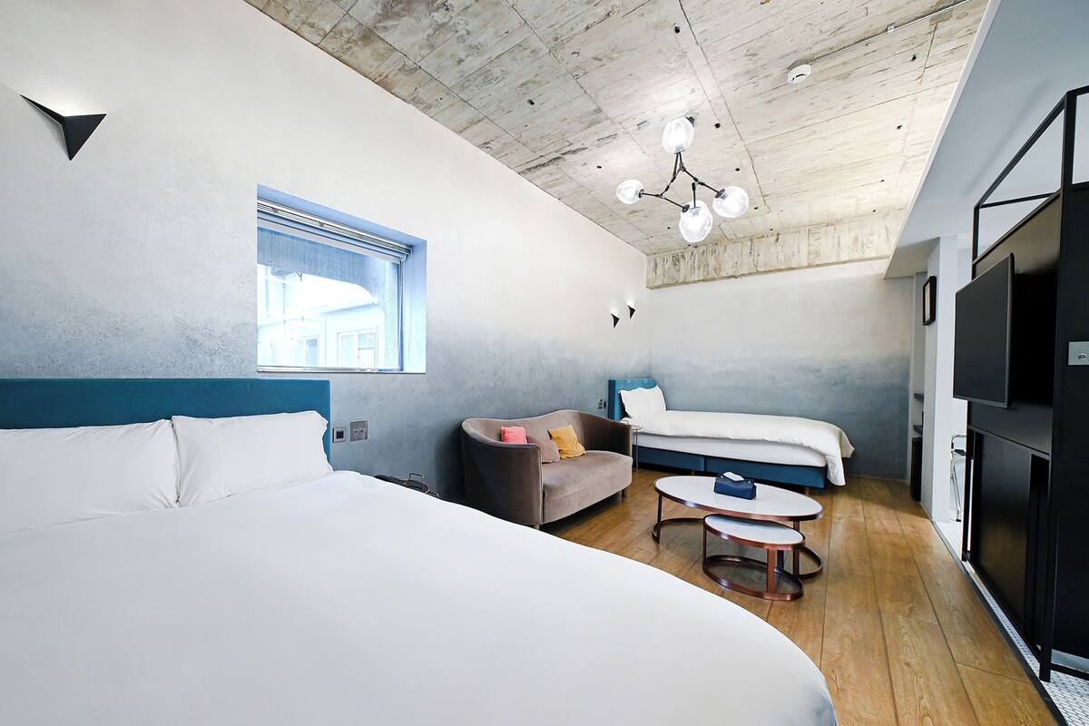 Una habitación de hotel moderna con una cama grande, un sofá, una mesita y un televisor.