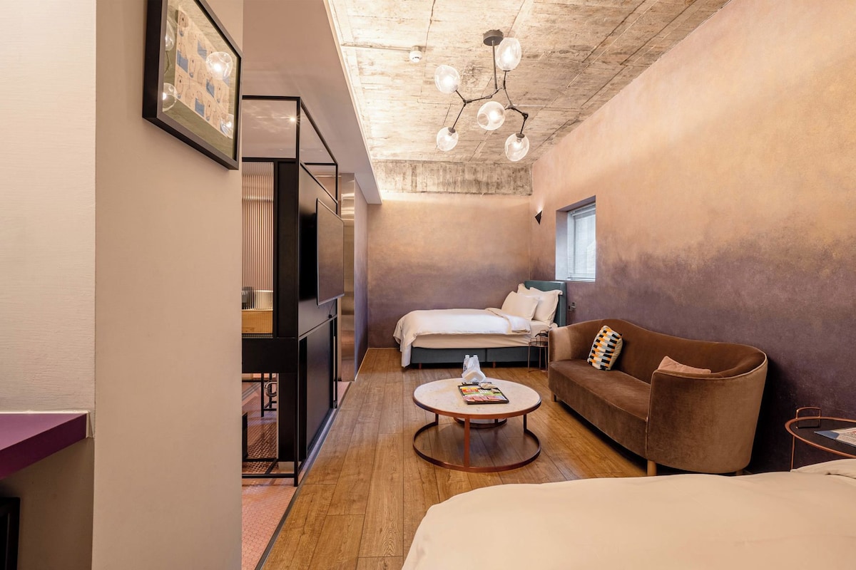 A modern hotel room with a bed, a sofa, a coffee table, and a TV.