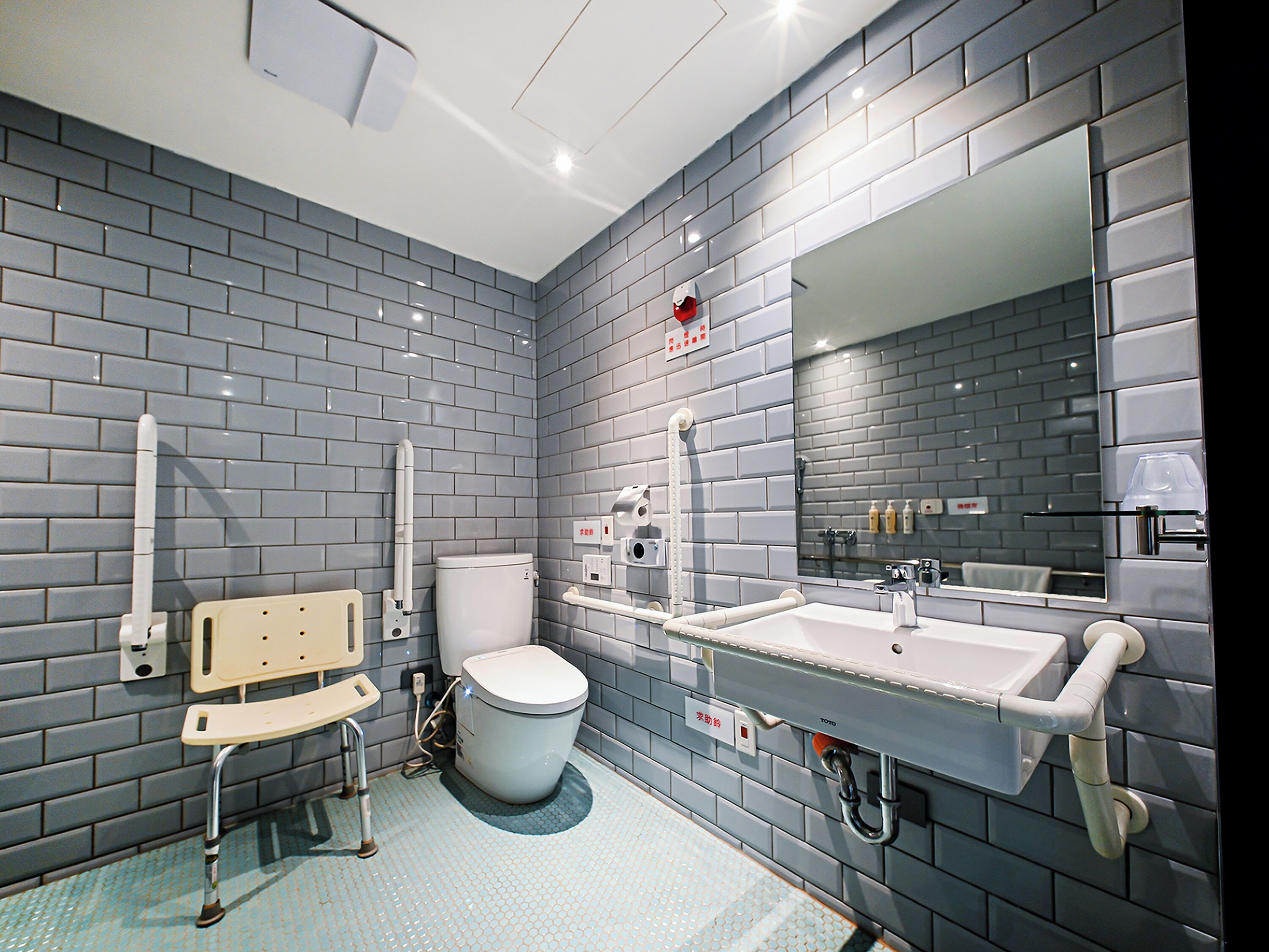 A modern bathroom with grey tiled walls, a white toilet, a sink, and a mirror.