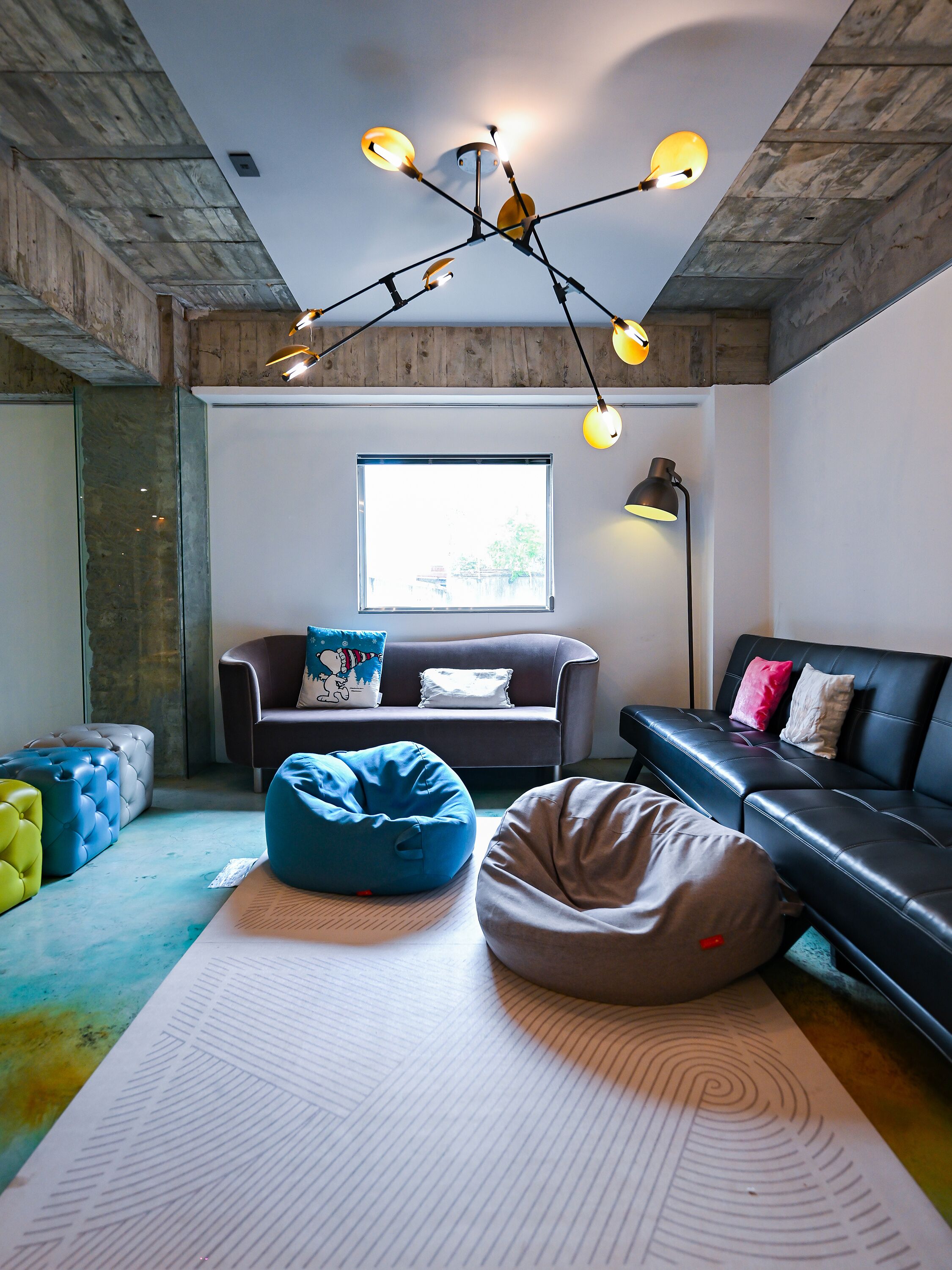 Una sala de estar moderna con un sofá de cuero negro, pufs azules y beige, un tapiz estampado y una lámpara de techo original.