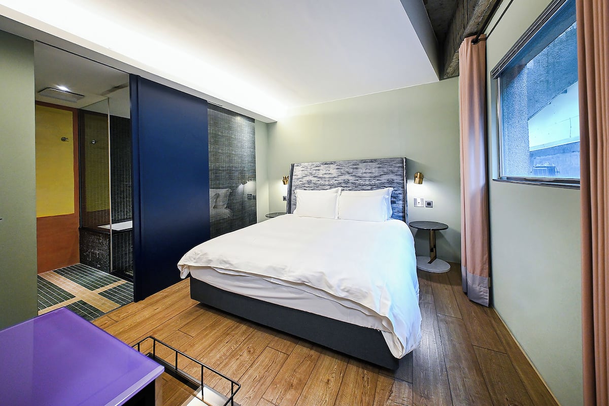 Habitación de hotel moderna con una cama grande, una mesita, un vestidor y una ventana con cortinas.