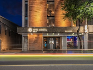 A hotel with a brick facade, a neon sign, and a tree in front. - Check inn Hive (Luodong)