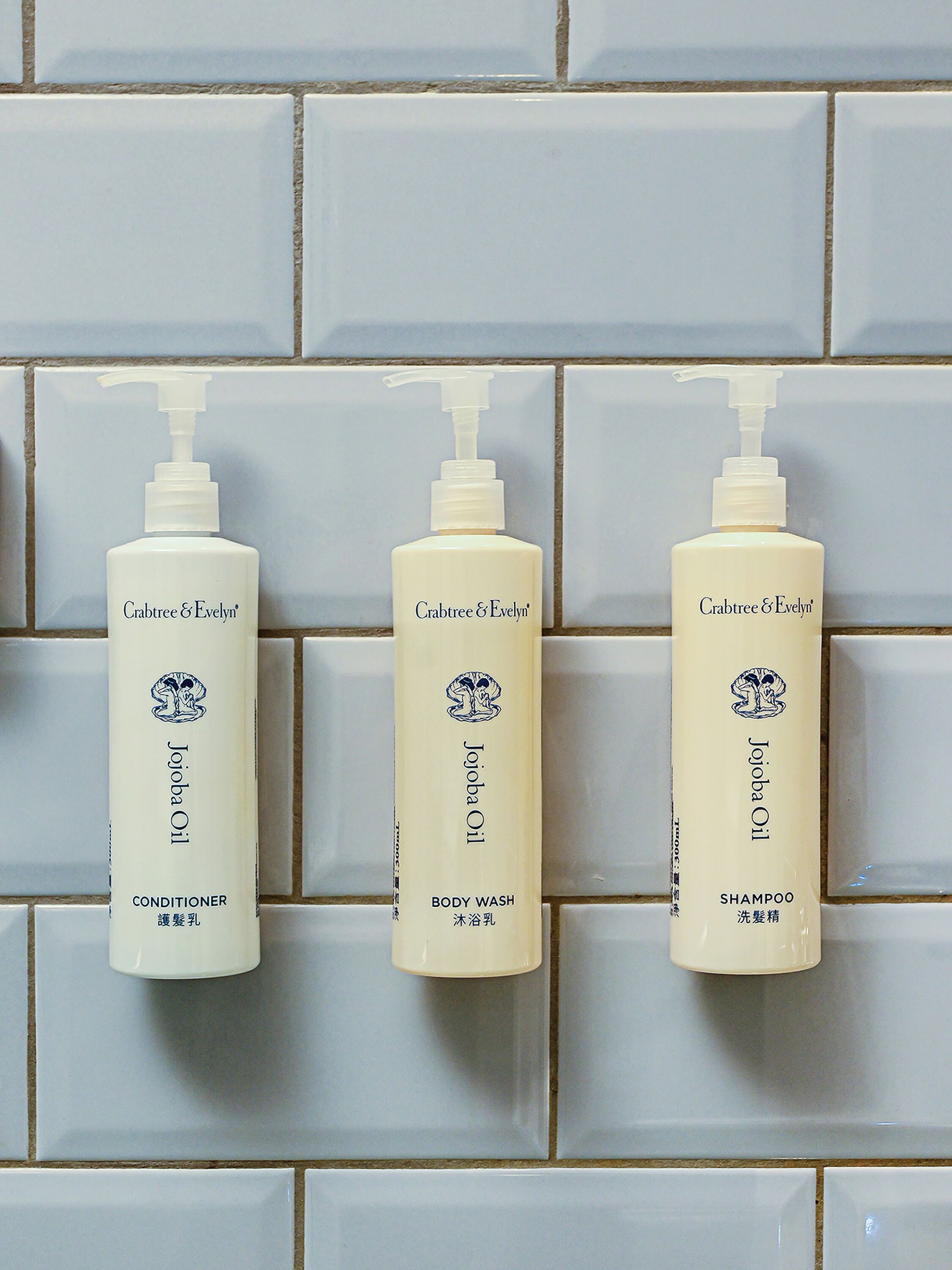 Three bottles of Crabtree & Evelyn products against a tiled wall.