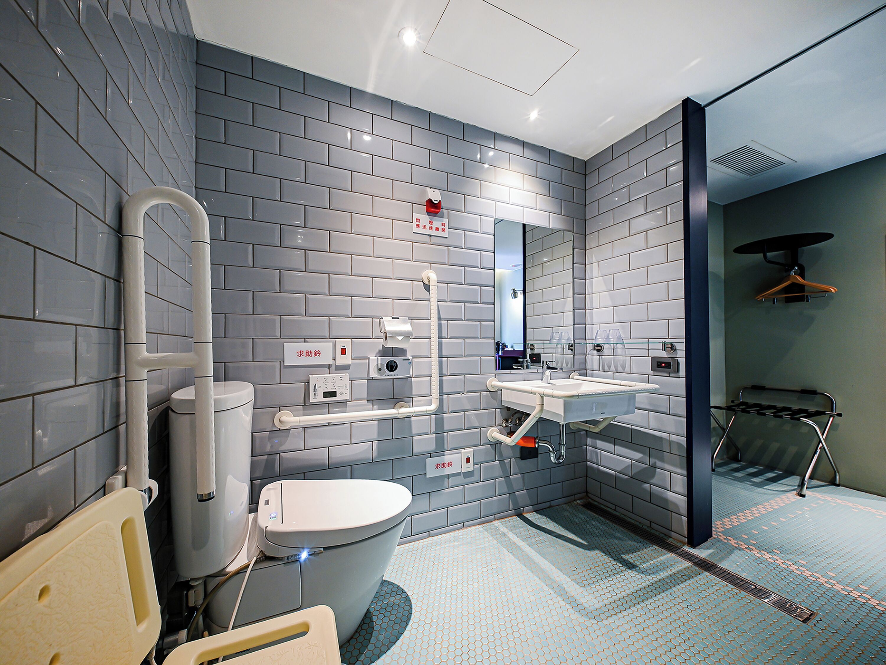 A modern bathroom with grey tiled walls, a toilet, a sink, and a shower area.