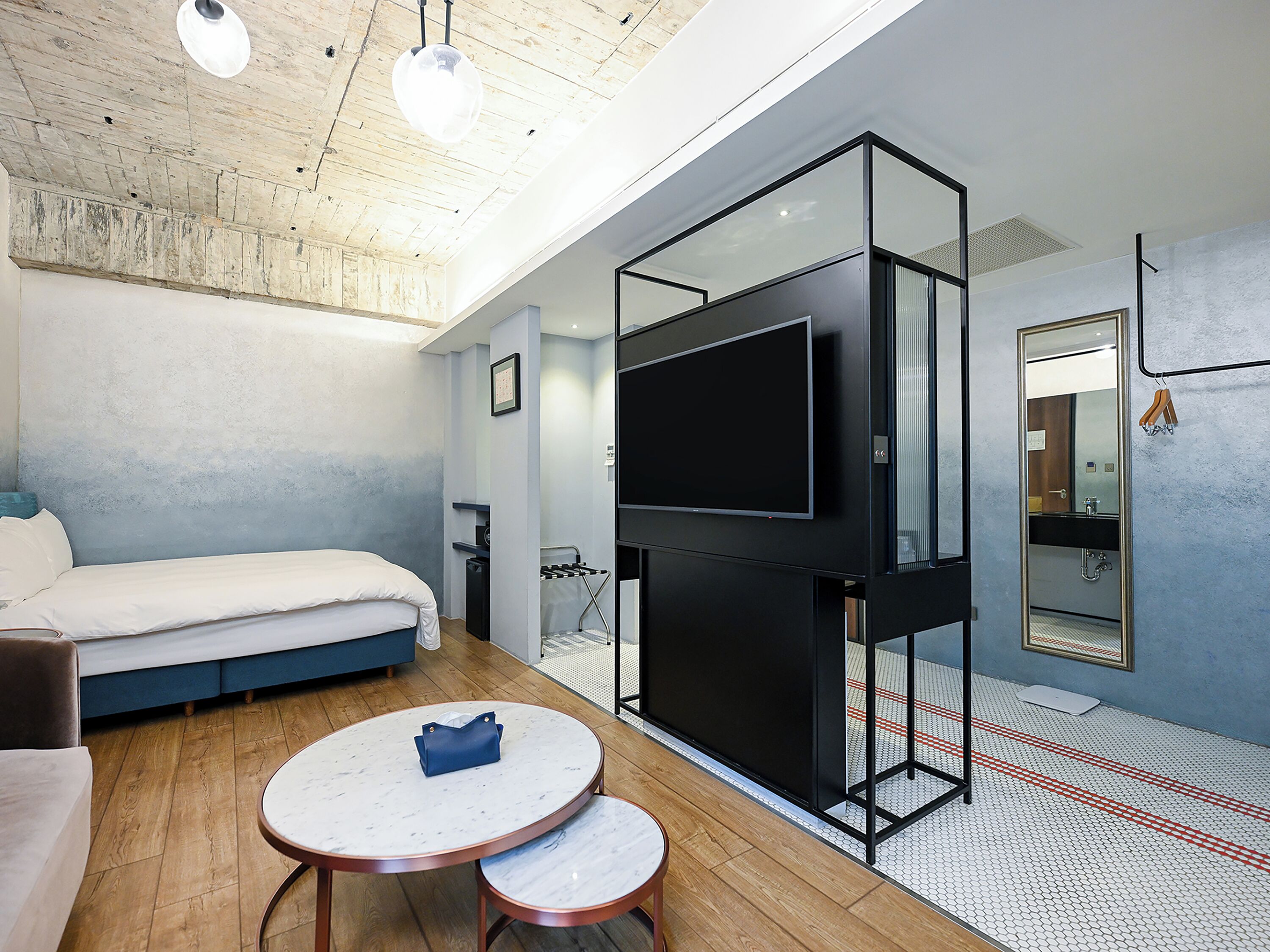 Una habitación de hotel moderna con cama, televisión, una mesita y baño con espejo y lavamanos.