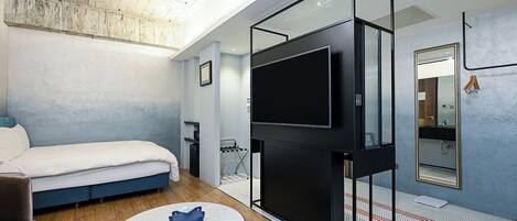Una habitación de hotel moderna con cama, televisión, una mesita y baño con espejo y lavamanos.
