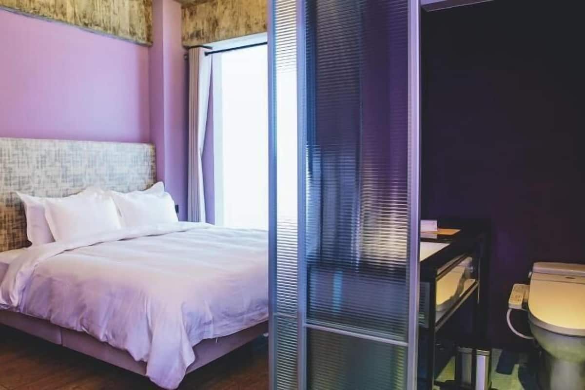 Un dormitorio con cama, escritorio, silla, inodoro y ventana con persianas.