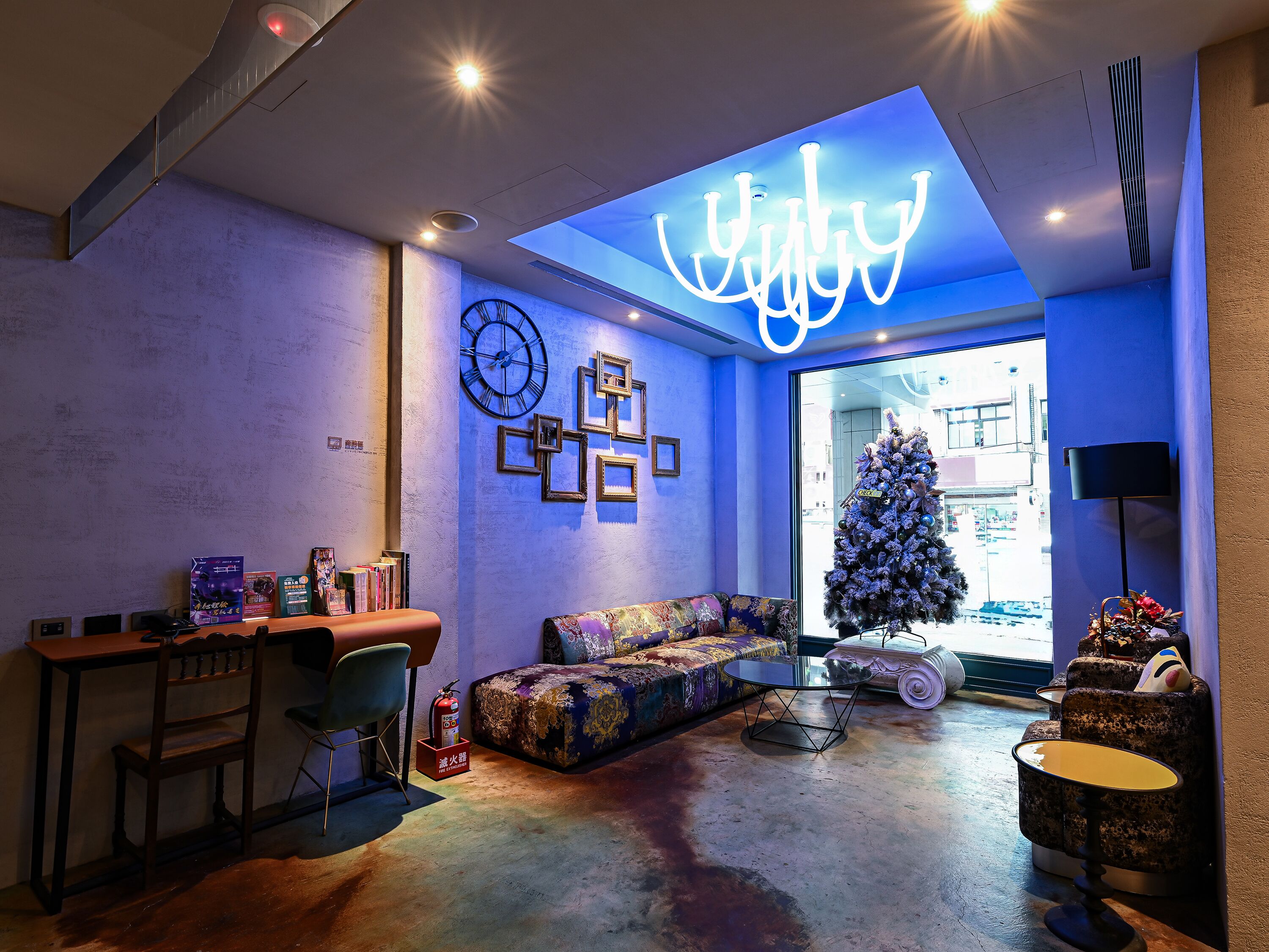 A modern living room with a sofa, a small table, a coffee table, a fireplace, a Christmas tree, and a neon sign.