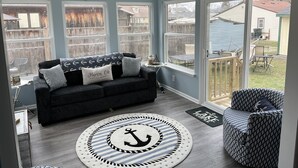 A living room with a dark gray sofa, a round rug with an anchor design, and a view of a backyard through large windows. - Beach Access! Minutes From Cedar Point, Kalahari, Jet Express, And Boat Basin! (Huron)