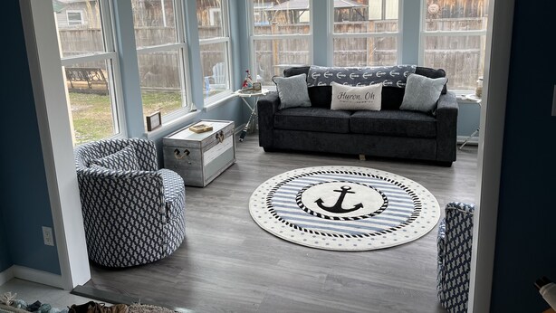 A cozy living room with a grey sofa, patterned ottoman, and a round rug with an anchor design. - Beach Access! Minutes From Cedar Point, Kalahari, Jet Express, And Boat Basin! (Huron)