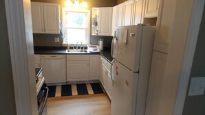 A compact kitchen with white cabinets, a black and white striped floor, and a refrigerator with magnets. - Beach Access! Minutes From Cedar Point, Kalahari, Jet Express, And Boat Basin! (Huron)