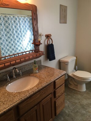 A bathroom with a granite countertop sink, wooden vanity, a mirror, a towel rack, and a toilet. - Beach Access! Minutes From Cedar Point, Kalahari, Jet Express, And Boat Basin! (Huron)