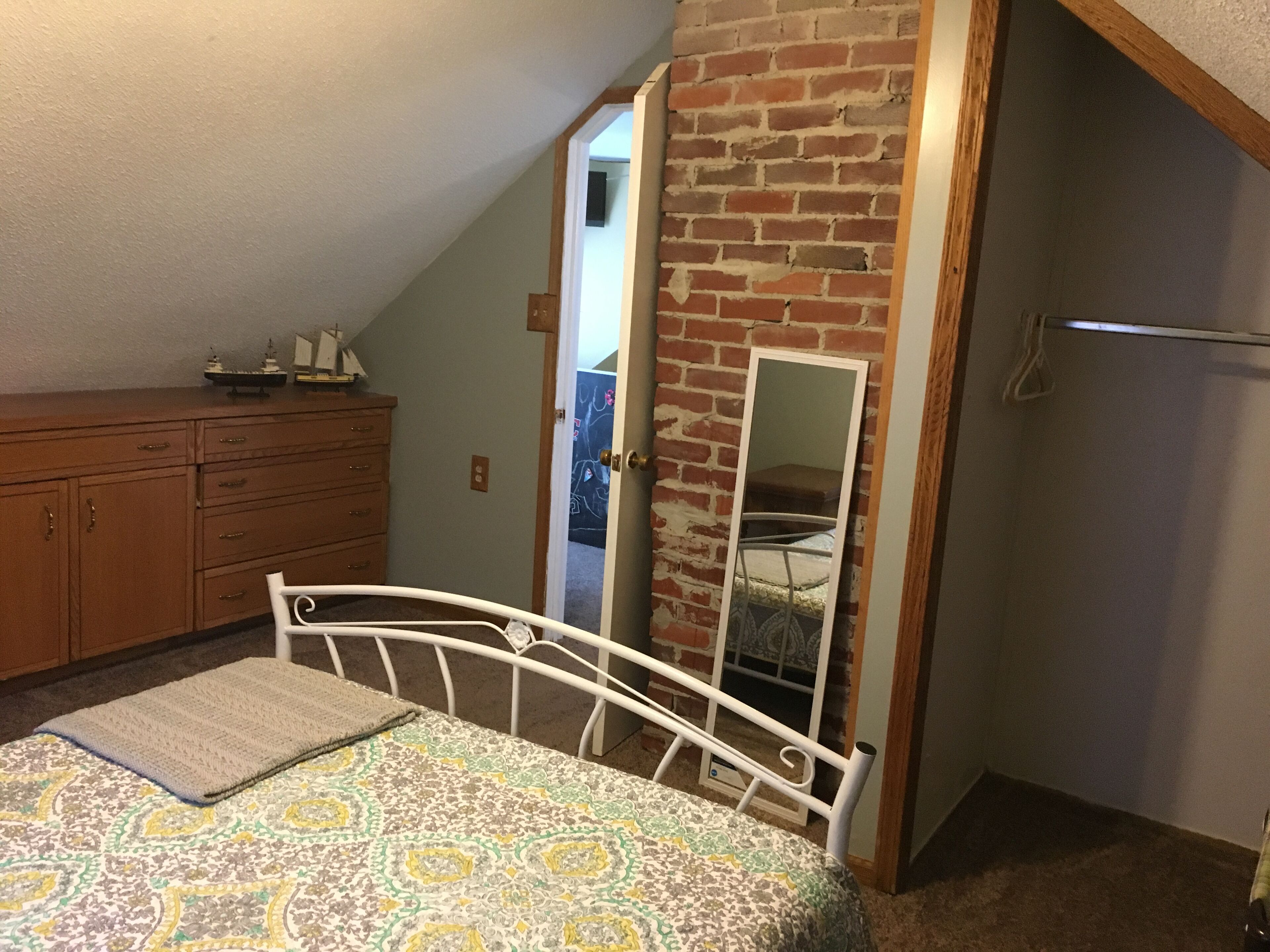 A bedroom with a bed, dresser, and a brick wall.