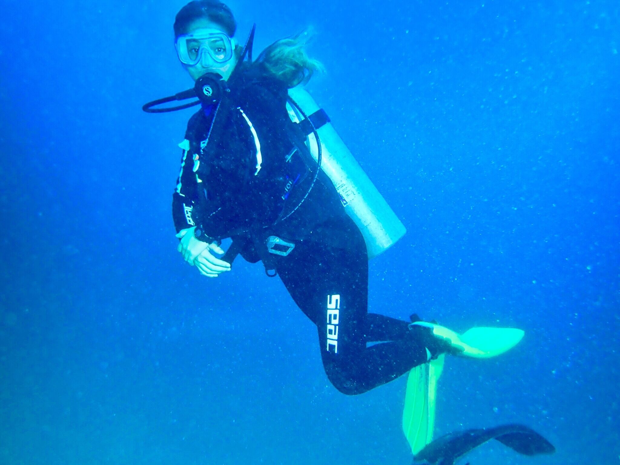 A diver in a wetsuit with a brand name on the leg, swimming underwater.
