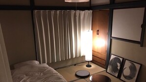 A traditional Japanese-style room with tatami flooring, a futon bed, a shoji screen, a standing lamp, and artwork on the walls. - Rengeso (Tokyo)