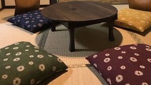 A room with tatami flooring, a round wooden table, and several cushions with floral patterns. - Rengeso (Tokyo)